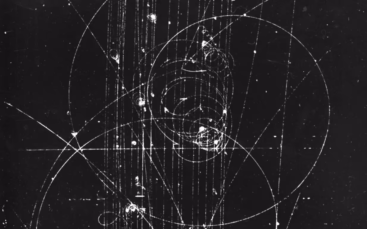 A bubble-chamber photograph: particle tracks curl into tight spirals across a field of straight beam tracks.